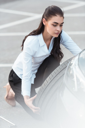 Young attractive woman in formal wear holding a spare car tire in parking lotの写真素材
