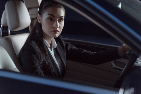 Young beautiful woman in suit sitting in a drivers seat of passenger carの写真素材