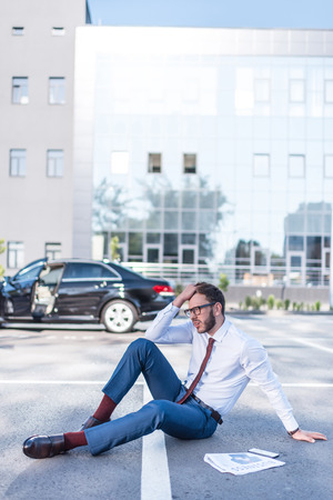 stressed businessman with newspaper sitting on parking with car behindの写真素材
