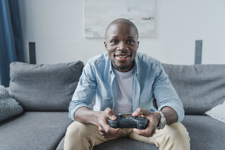 African american man playing video game with joystick at homeの写真素材