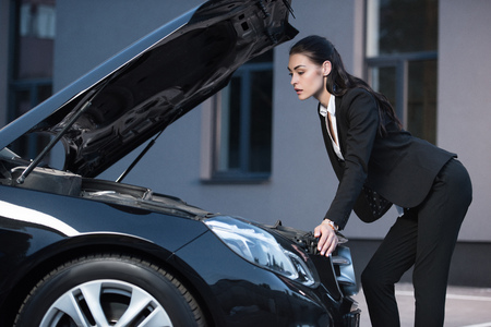 Young attractive businesswoman looking under an open hood of passenger carの写真素材