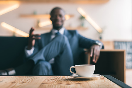 selective focus of african american businessman sitting with cup of coffee in cafe の写真素材