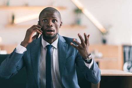 shocked handsome african american businessman gesturing and talking on smartphoneの写真素材