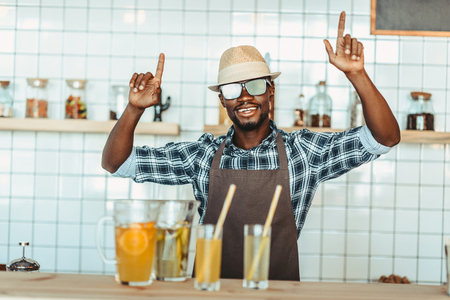 cheerful stylish african american bartender gesturing and standing at bar counter with lemonades  の写真素材
