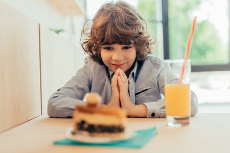 excited little boy looking on piece cake while sitting in cafeの写真素材
