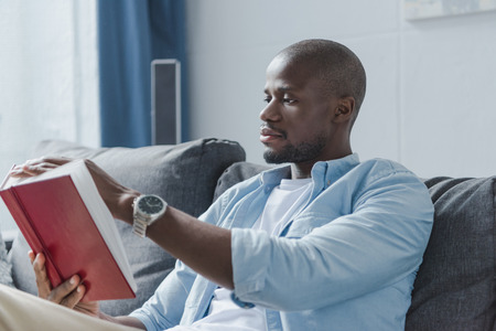 Handsome african american man reading book at home