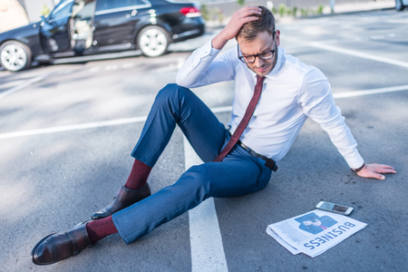 stressed businessman with newspaper and smartphone sitting on parking with car behindの写真素材