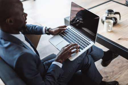 handsome african american businessman working with laptop with blank screen in cafe の写真素材