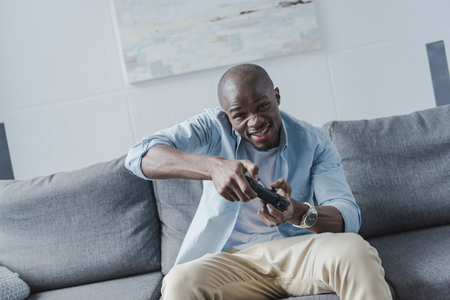 African american man playing video game with joystick at homeの写真素材
