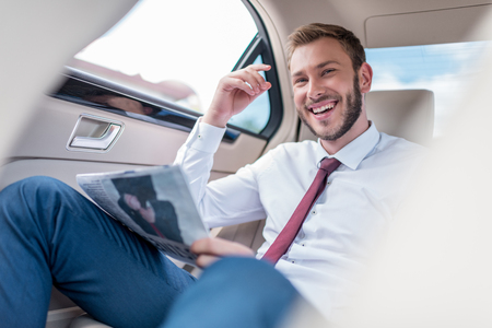 happy young man with newspaper on backseat of car