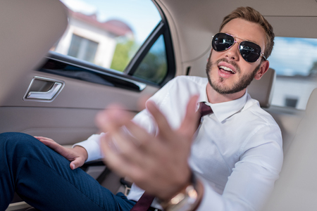 young stylish businessman in sunglasses on backseat of carの写真素材