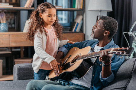 African american man playing guitar with his cute daughterの写真素材