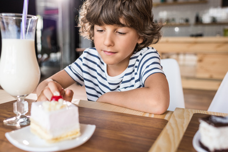 cute little boy with piece of cake in cafeの写真素材