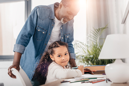 African american man helping his daughter drawing picture with colorful markersの写真素材