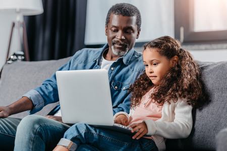 adorable african american girl using laptop together with father at homeの写真素材
