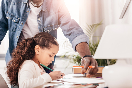 Cropped image of man helping his african american daughter drawing picture with colorful markersの写真素材