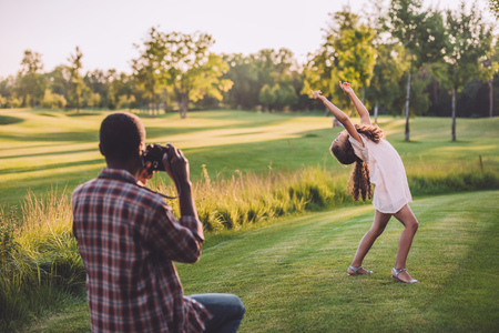 african american man taking photo of his granddaughter playing on green lawn の写真素材