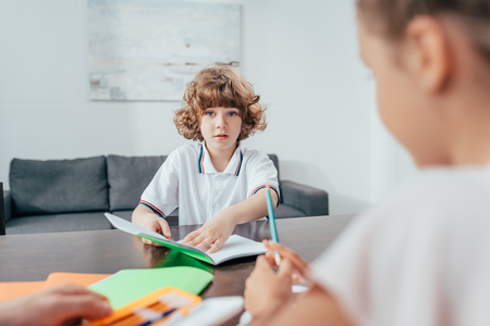 adorable curly boy doing homework with sister blurred on foregroundの写真素材