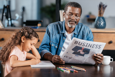 Adorable african american girl drawing while her father reading newspaperの写真素材