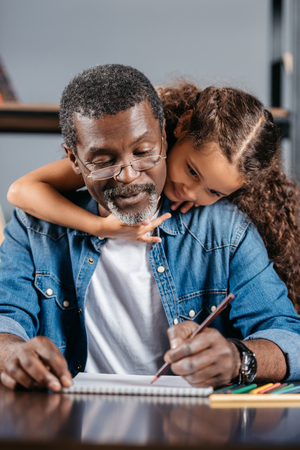 African american man sitting at table and drawing picture with daughterの写真素材