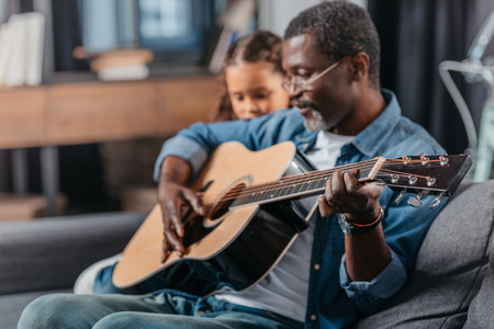 African american man playing guitar with his cute daughterの写真素材
