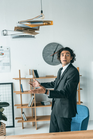 side view of young emotional businessman throwing folders with documents in officeの写真素材