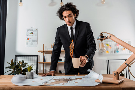 portrait of businessman accidentally pouring coffee on blueprints at workplace in office の写真素材