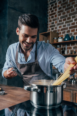 handsome young man with apron cooking pastaの写真素材