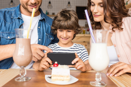 beautiful young family taking photo of dessert with smartphone in cafeの写真素材