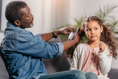 African american man combing hair of his daughter with combの写真素材