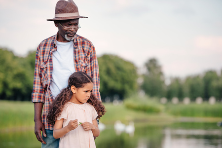 little african american granddaughter and her grandfather standing together in park の写真素材