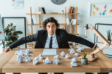 portrait of overworked businessman sitting at workplace full of crumpled documentsの写真素材