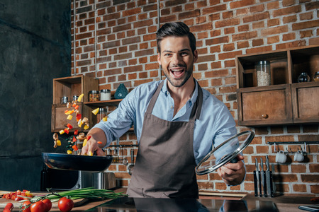 happy young man with apron frying peppersの写真素材