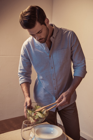 handsome young man putting salad on plateの写真素材