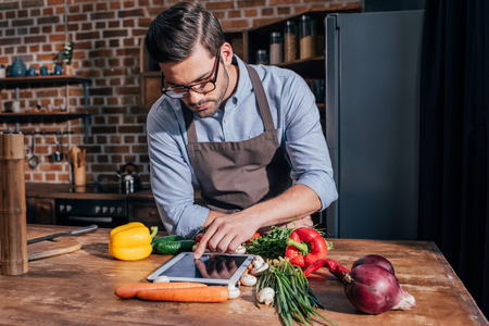 stylish young man in apron cooking with tabletの写真素材