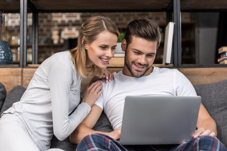 happy young couple using laptop while sitting on sofa at homeの写真素材