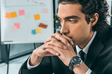 portrait of young pensive businessman in suit with hands in lock in officeの写真素材