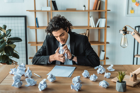 portrait of angry businessman crumpling papers at workplace in office
