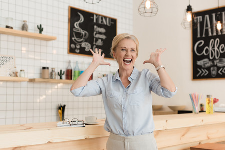 excited mature businesswoman gesturing with hands and looking away in cafeの写真素材