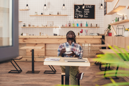 laughing african american man drinking coffee at table in cafeの写真素材
