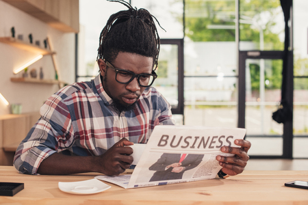 focused african american man drinking coffee and reading business newspaperの写真素材