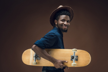 happy african american man holding skate isolated on brownの写真素材