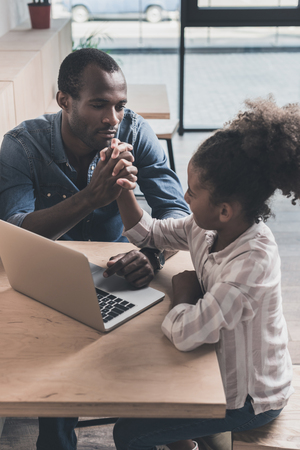 african-american father and adorable daughter sitting in cafe with laptopの写真素材