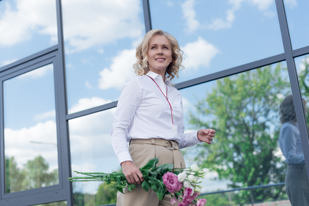 portrait of smiling caucasian woman with bouquet of fresh flowers looking awayの写真素材