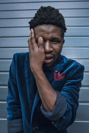 stylish african american man in blue jacket covering eye with hand