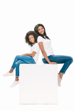 beautiful happy african american mother and daughter sitting together and smiling at camera isolated on white  の写真素材