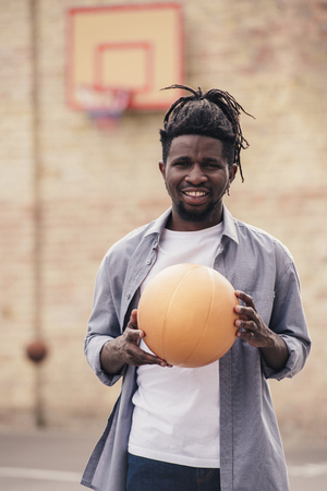smiling african american man holding basketball ball at streetの写真素材