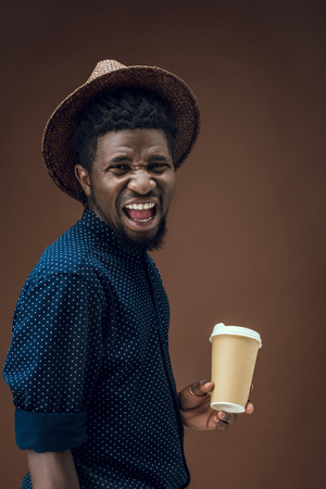 screaming african american man with disposable coffee cup isolated on brownの写真素材