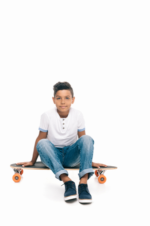 cute african american boy sitting on skateboard and looking at camera isolated on whiteの写真素材