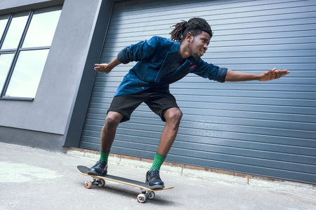 stylish african american man in blue jacket skating on streetの写真素材
